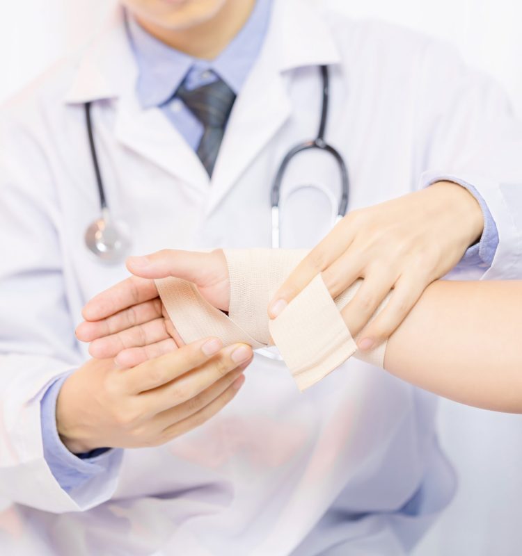 Male doctor putting gauze on young man's hand in clinic, closeup. First aid